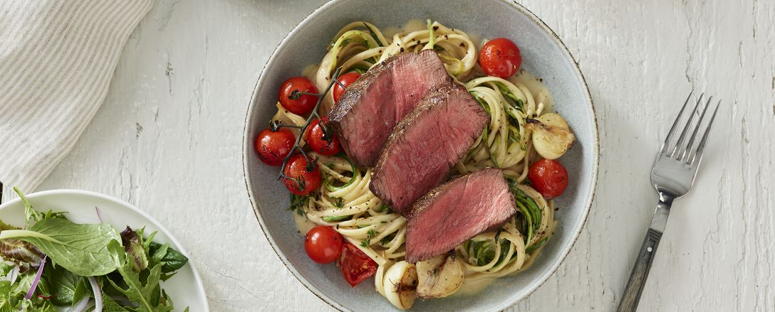 Medium rare steak served on pasta and tomatoes